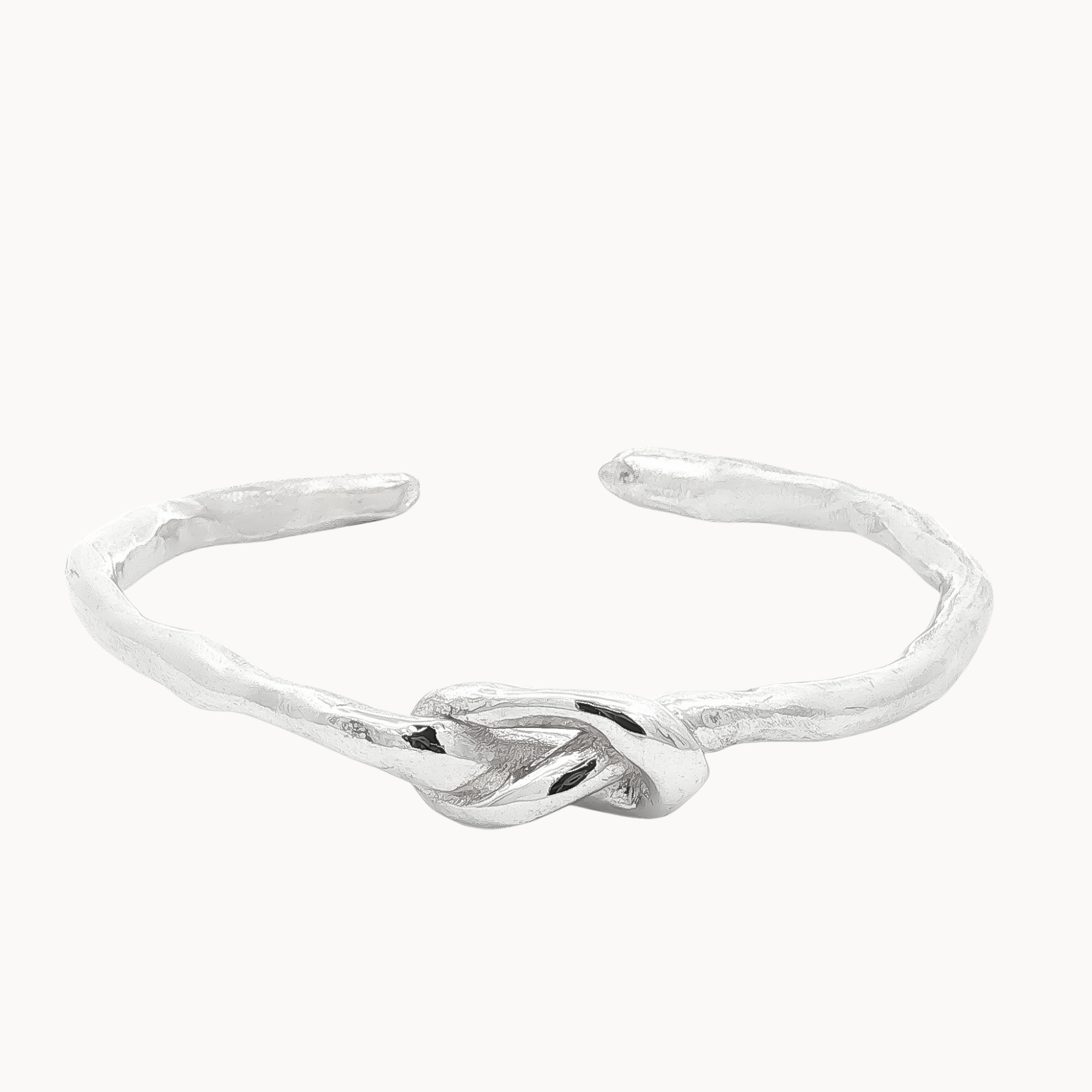 A textured sterling silver open cuff bangle featuring a central knotted design, shown on a plain off-white background.