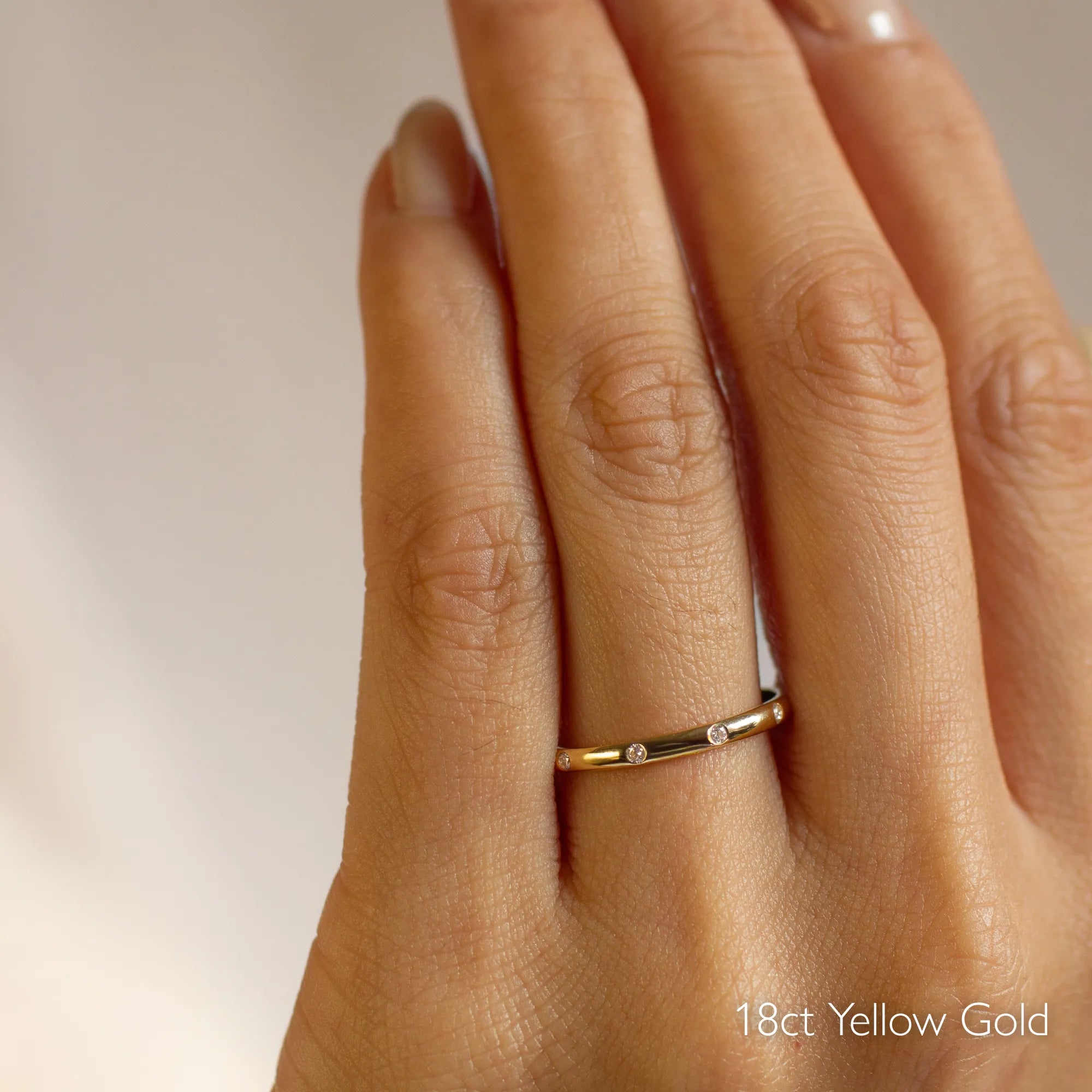 Gold wedding ring with small round diamonds on a hand with '18ct Yellow Gold' text
