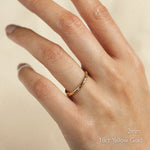 Hand wearing a 2mm wide 18ct yellow gold ring on a beige background