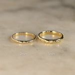 Two gold rings with diamonds and star engraving with '2mm' and '3mm' labels on a beige surface