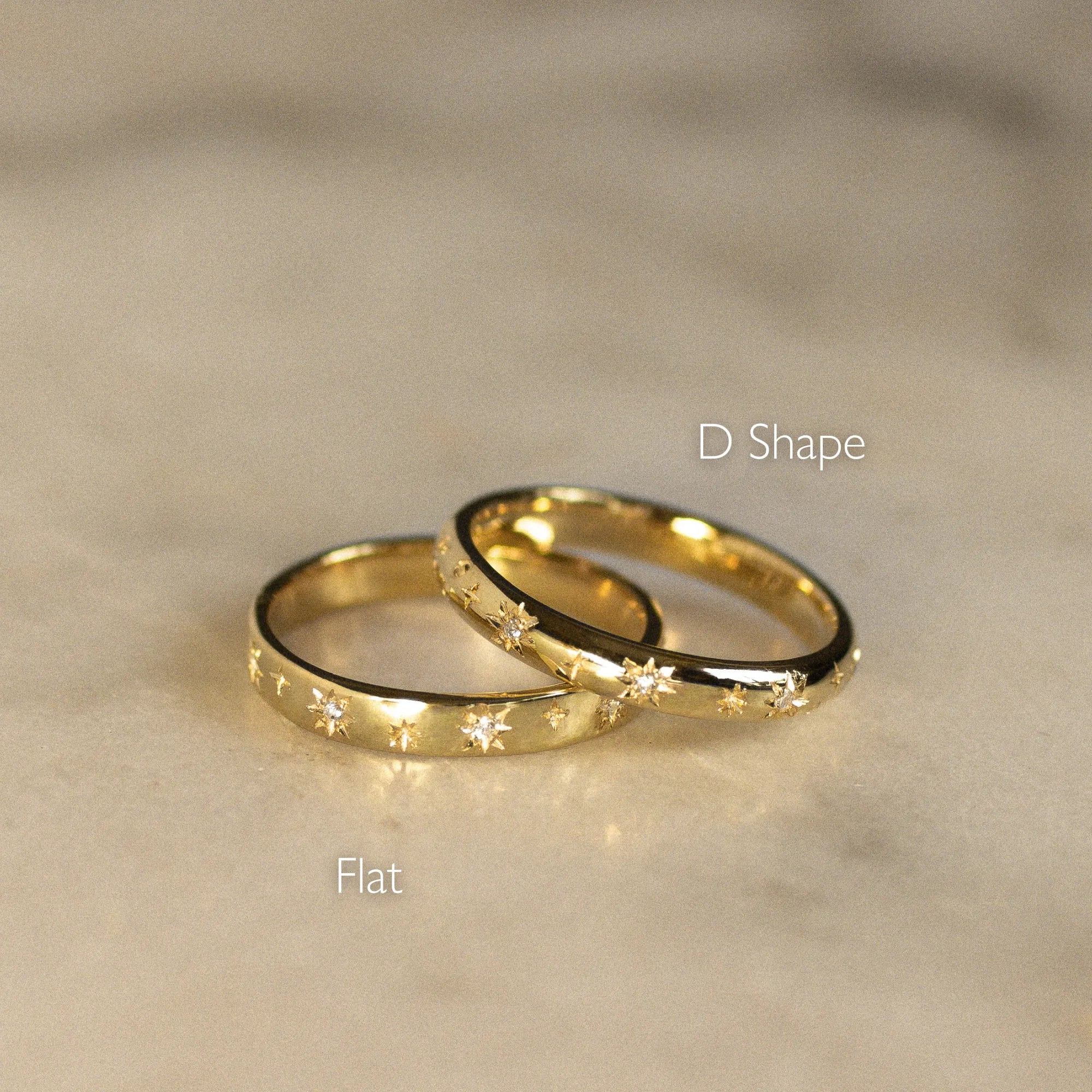 Two gold rings, one flat and one D-shaped, on a beige surface.