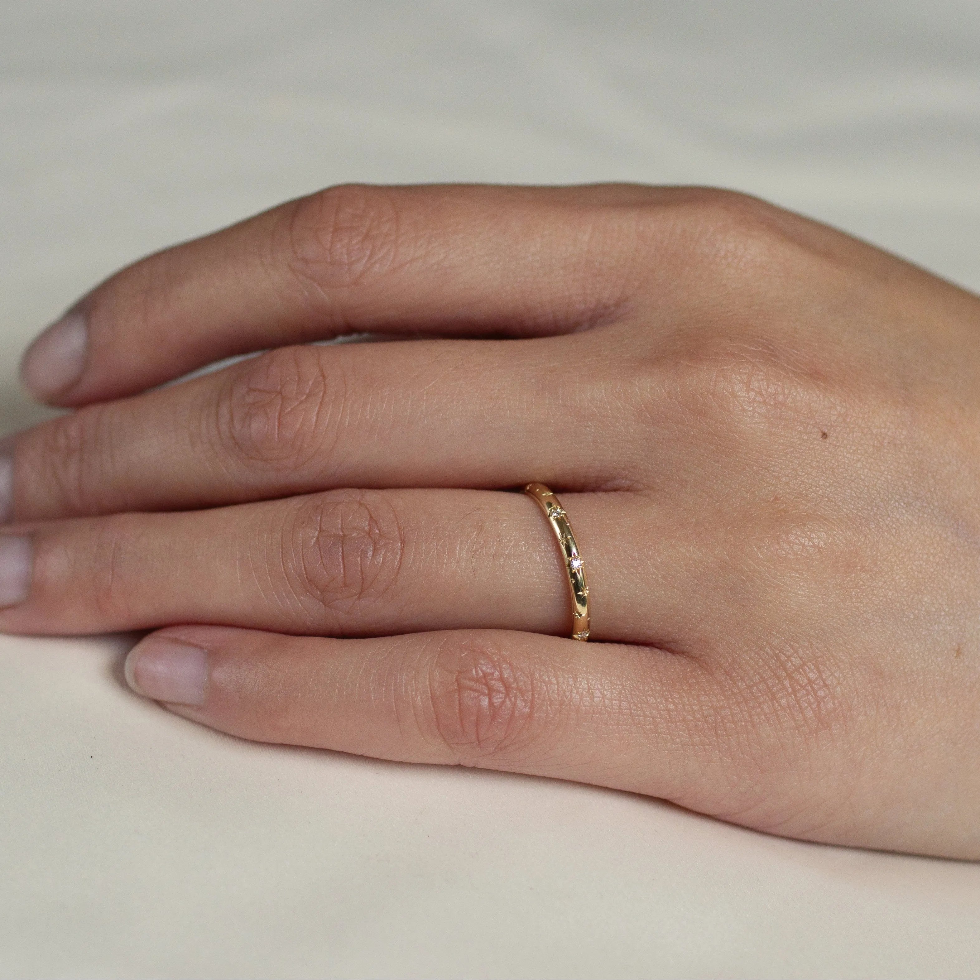 Close up of resting hand wearing solid 18ct gold wedding band with diamond and star detailing