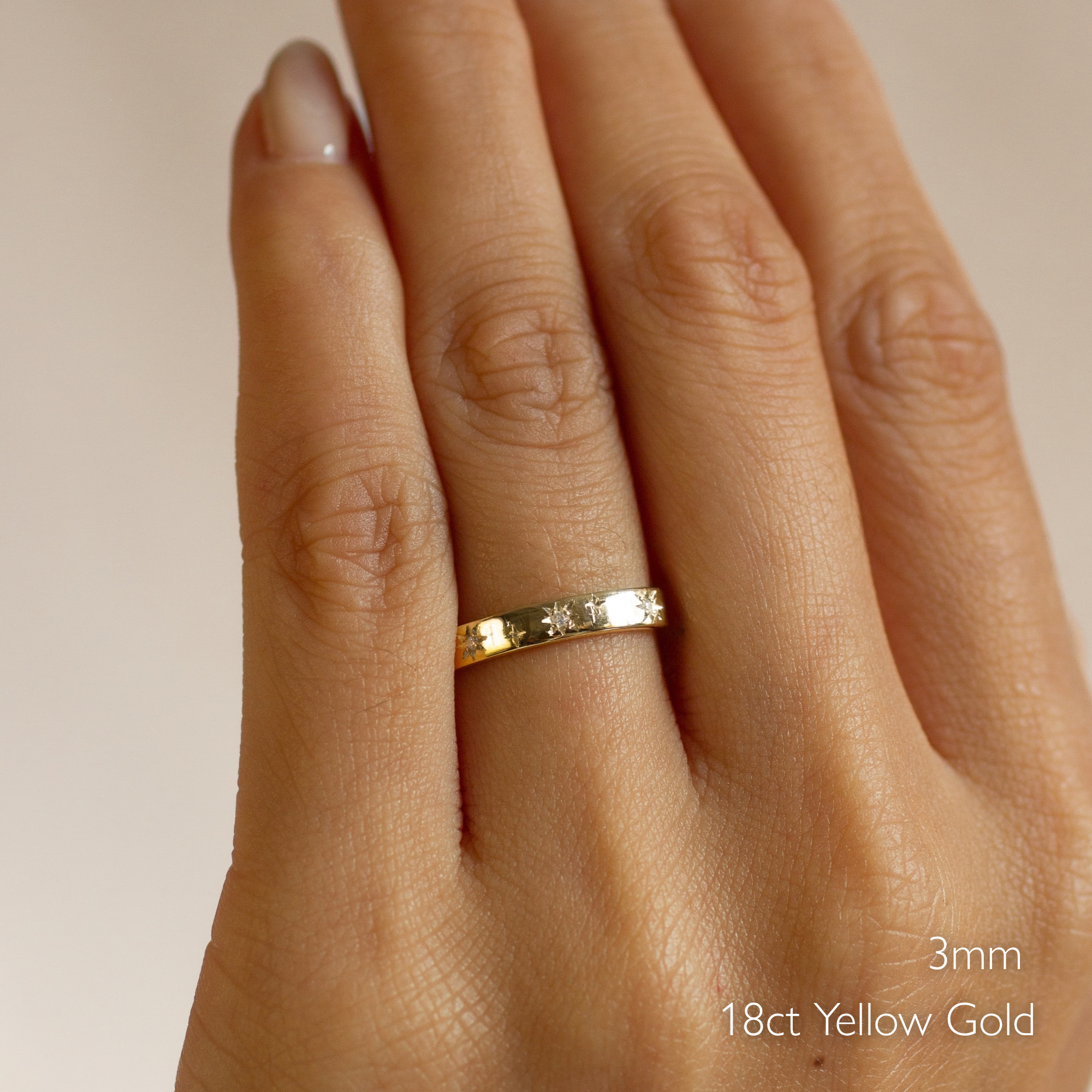 close up of a hand wearing a 3mm 18ct yellow gold flat wedding ring with star engraving and diamonds