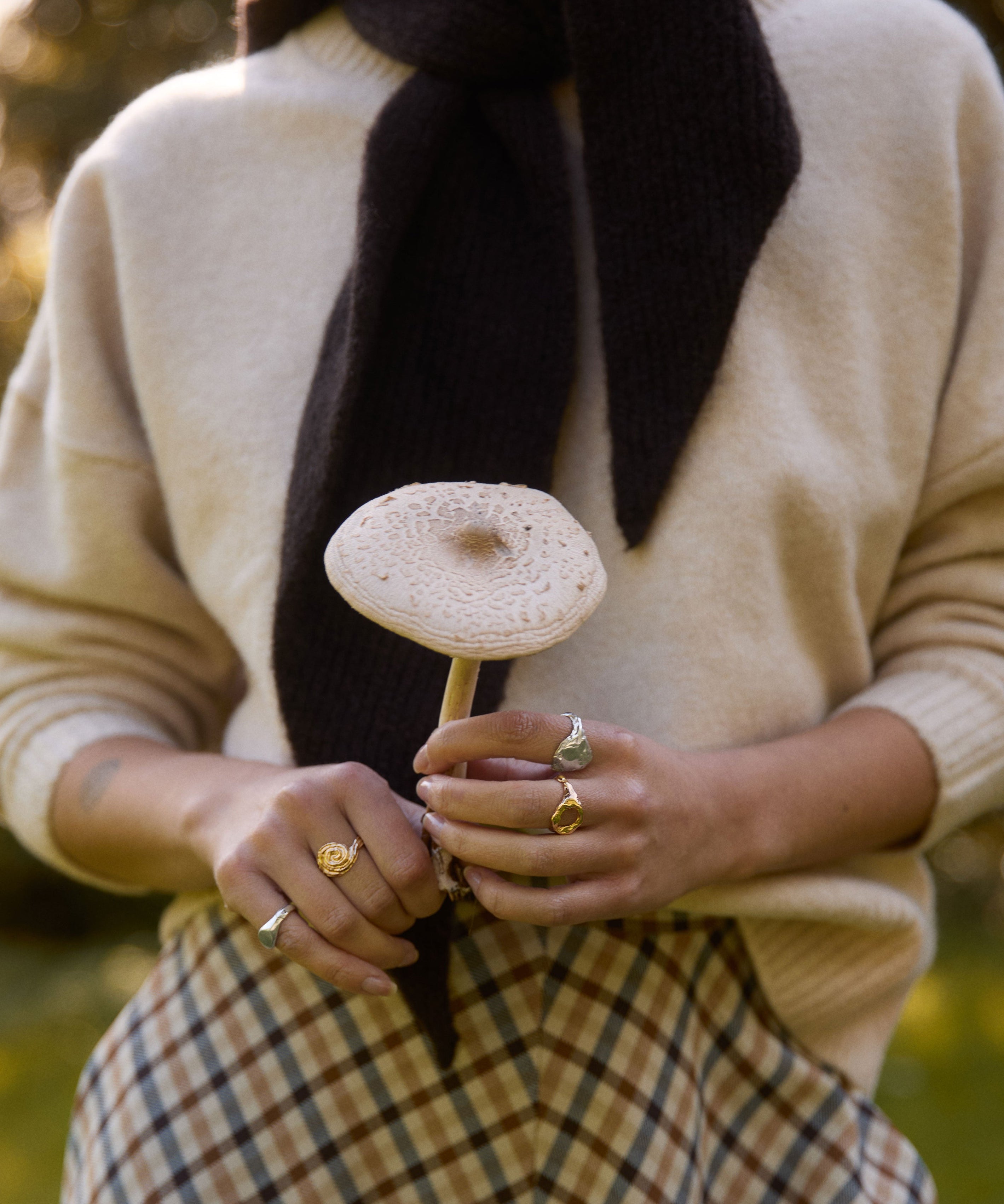 Person holding a mushroom and wearing rings with a blurred natural background