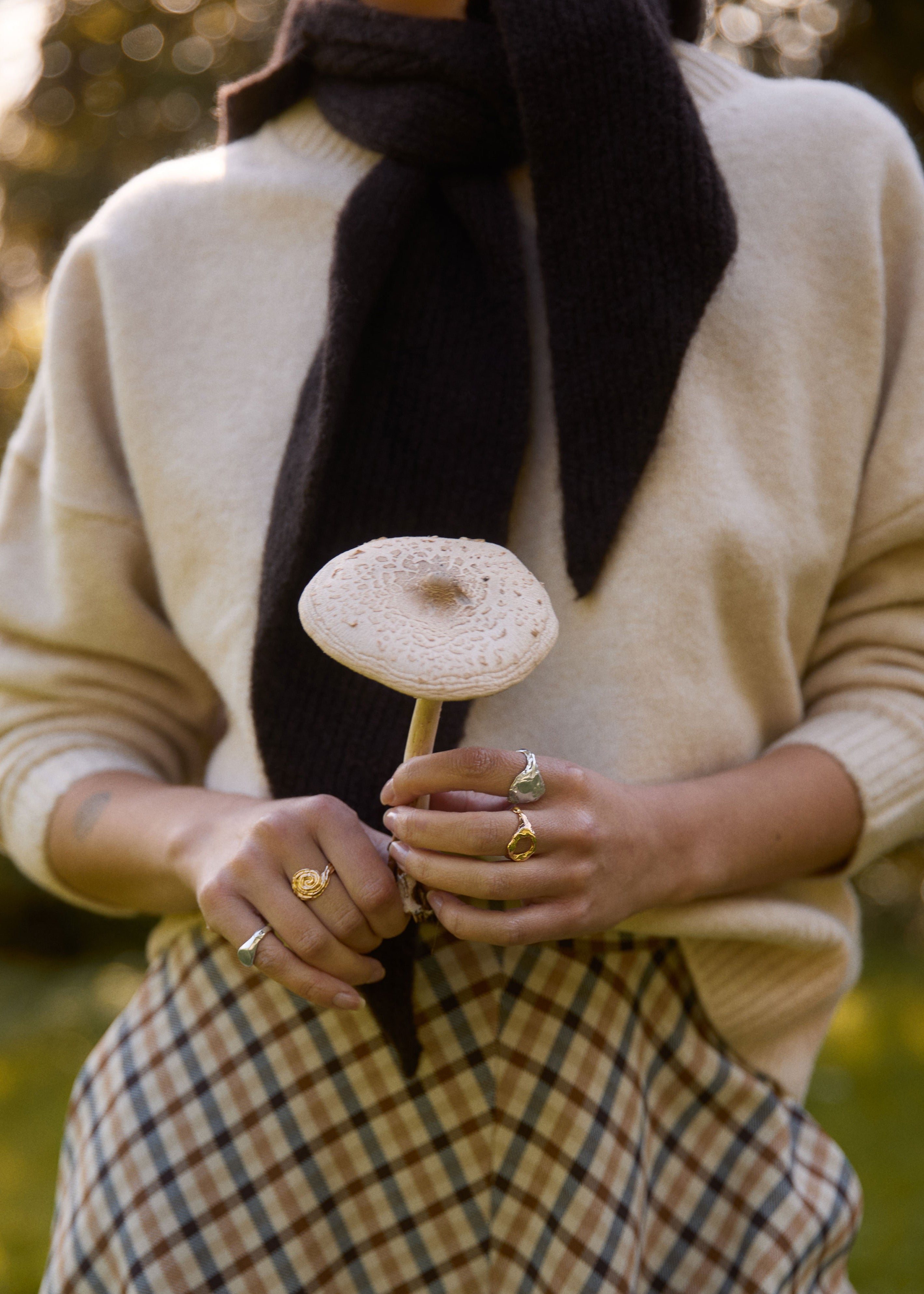 Person holding a mushroom and wearing rings with a blurred natural background