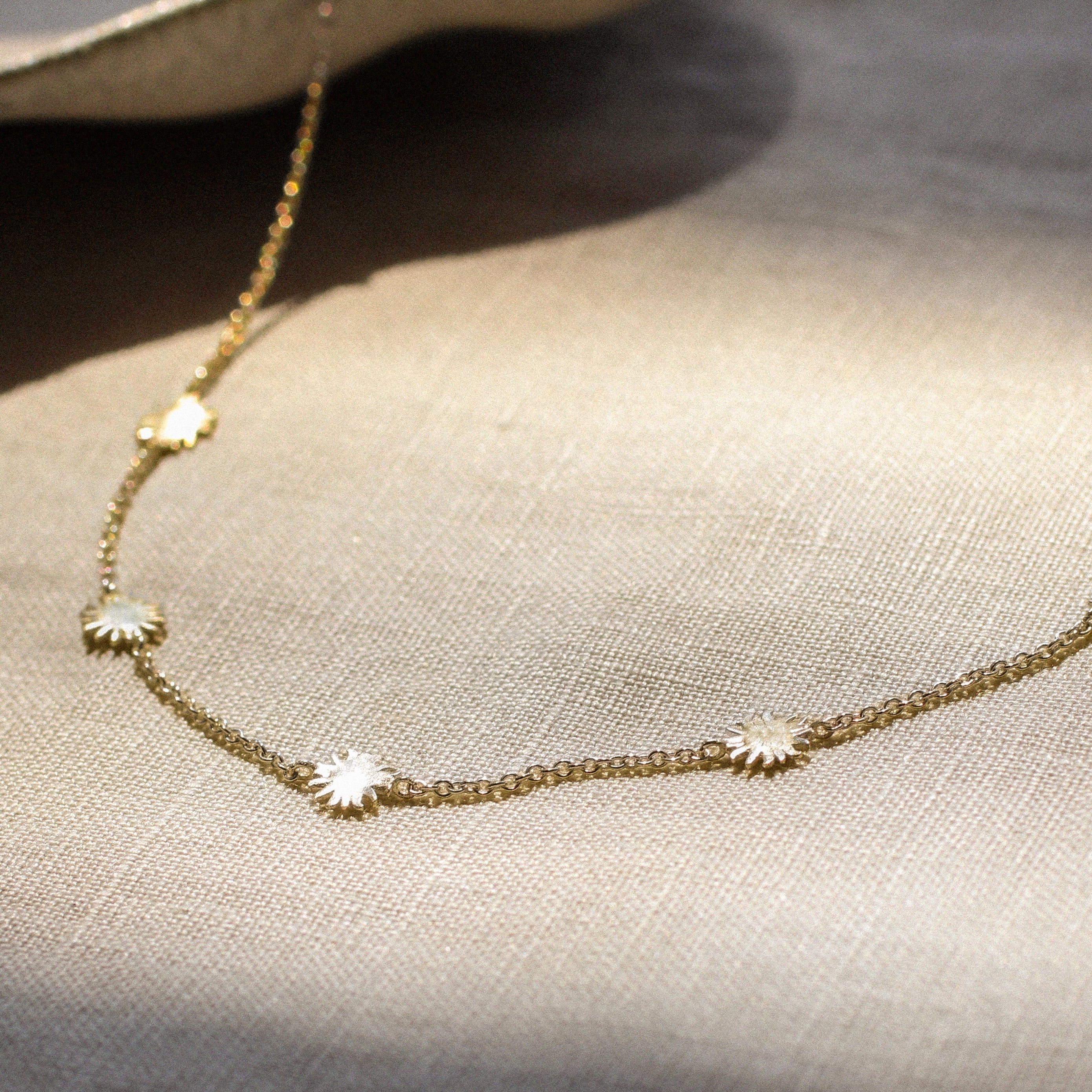 gold chain necklace with tiny sun shaped pendants on a fabric surface