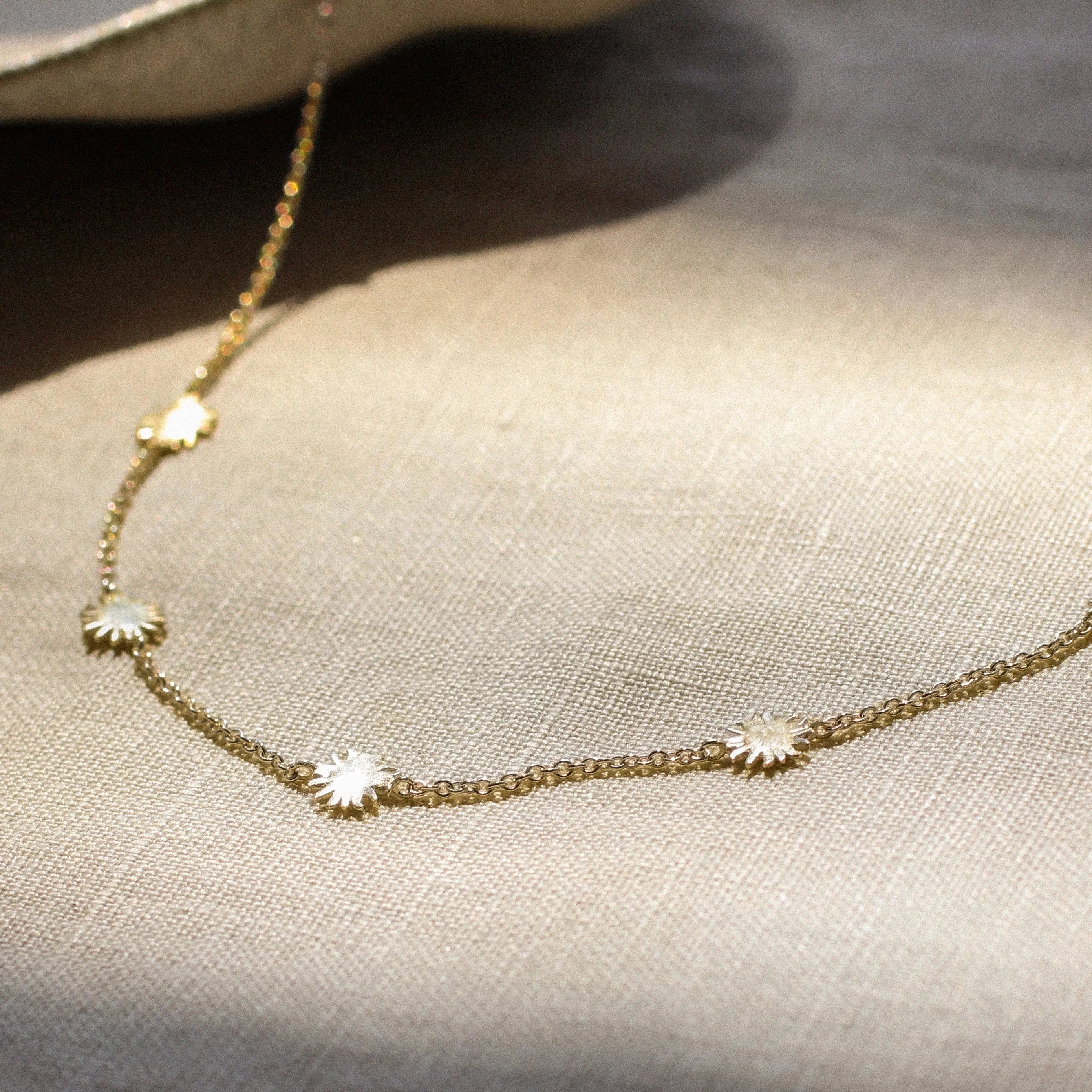 gold chain necklace with tiny sun shaped pendants on a fabric surface