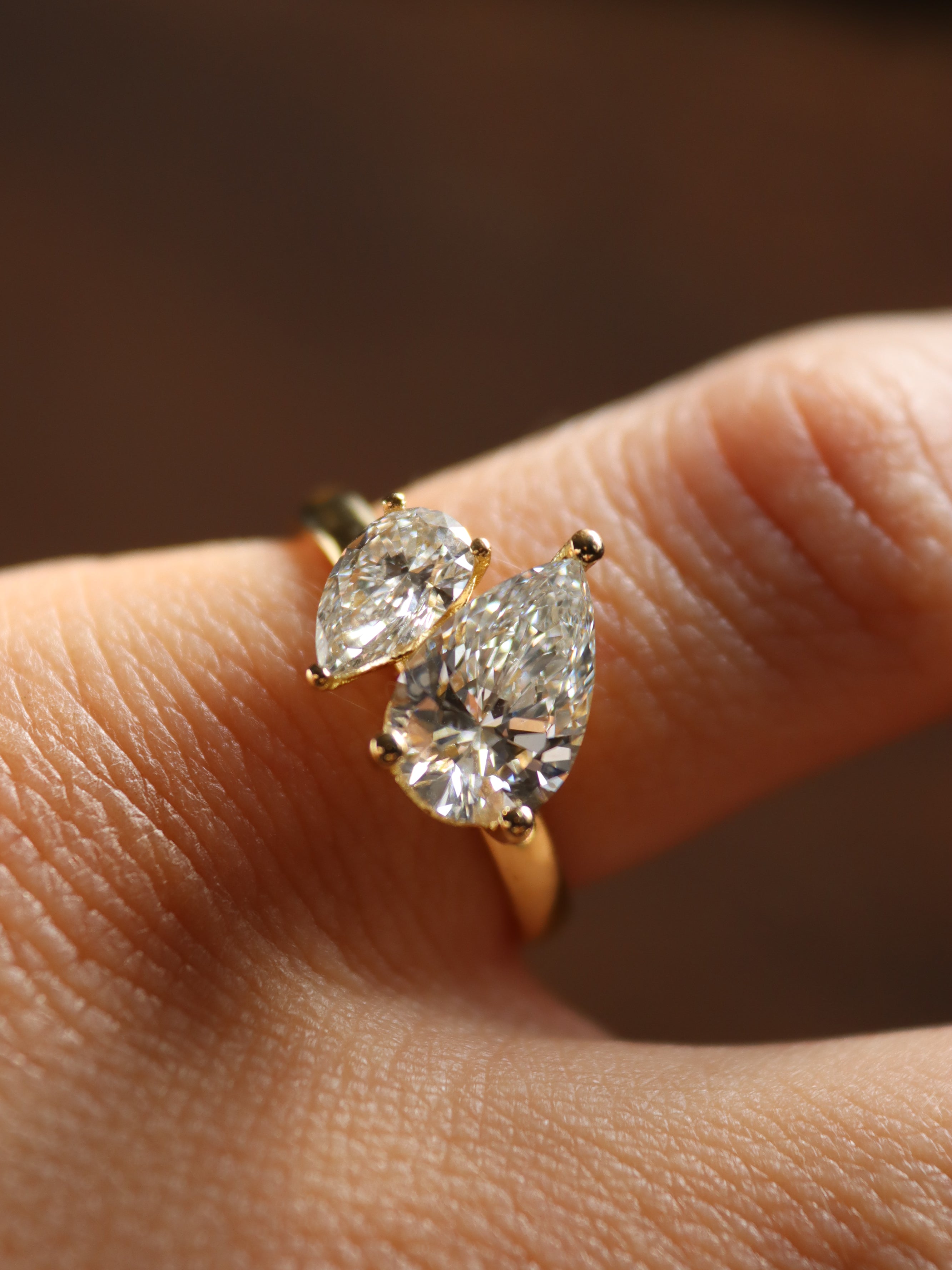 Gold toi et moi engagement ring with two pear-shaped diamonds on a finger against a blurred background