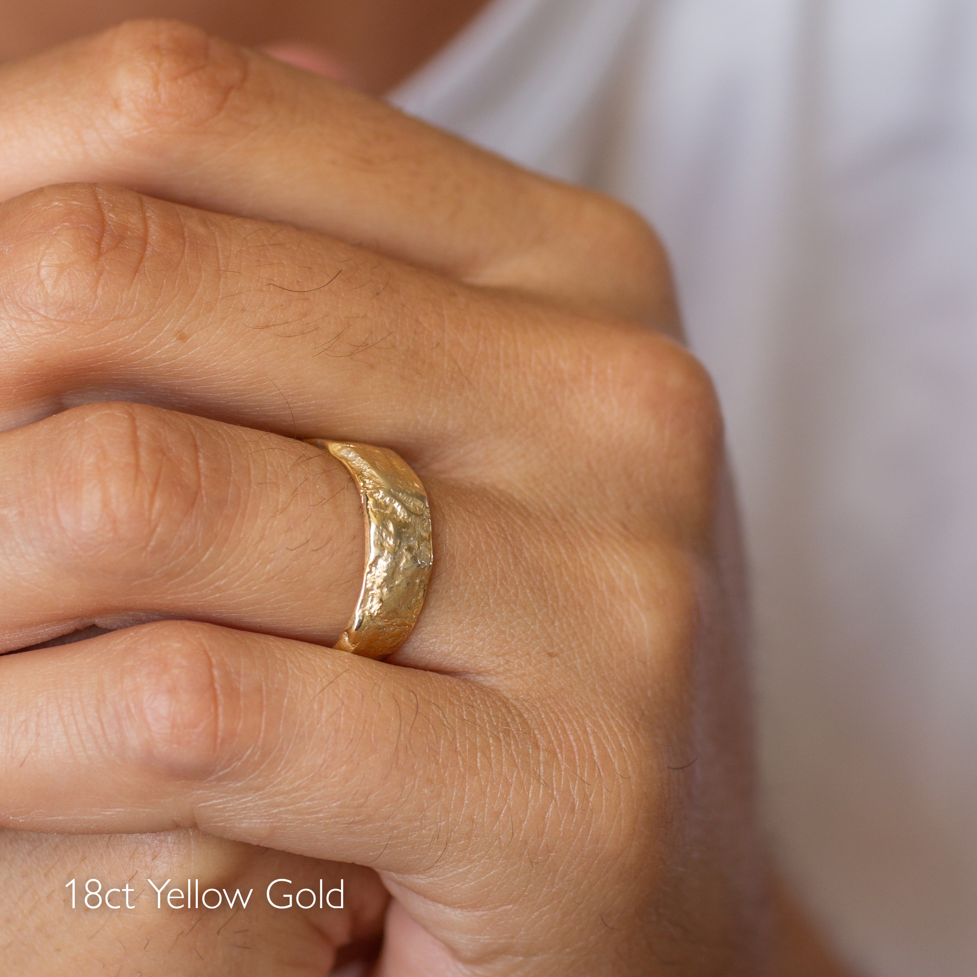 hand wearing tree bark textured wedding ring in 18ct yellow gold with blurred background