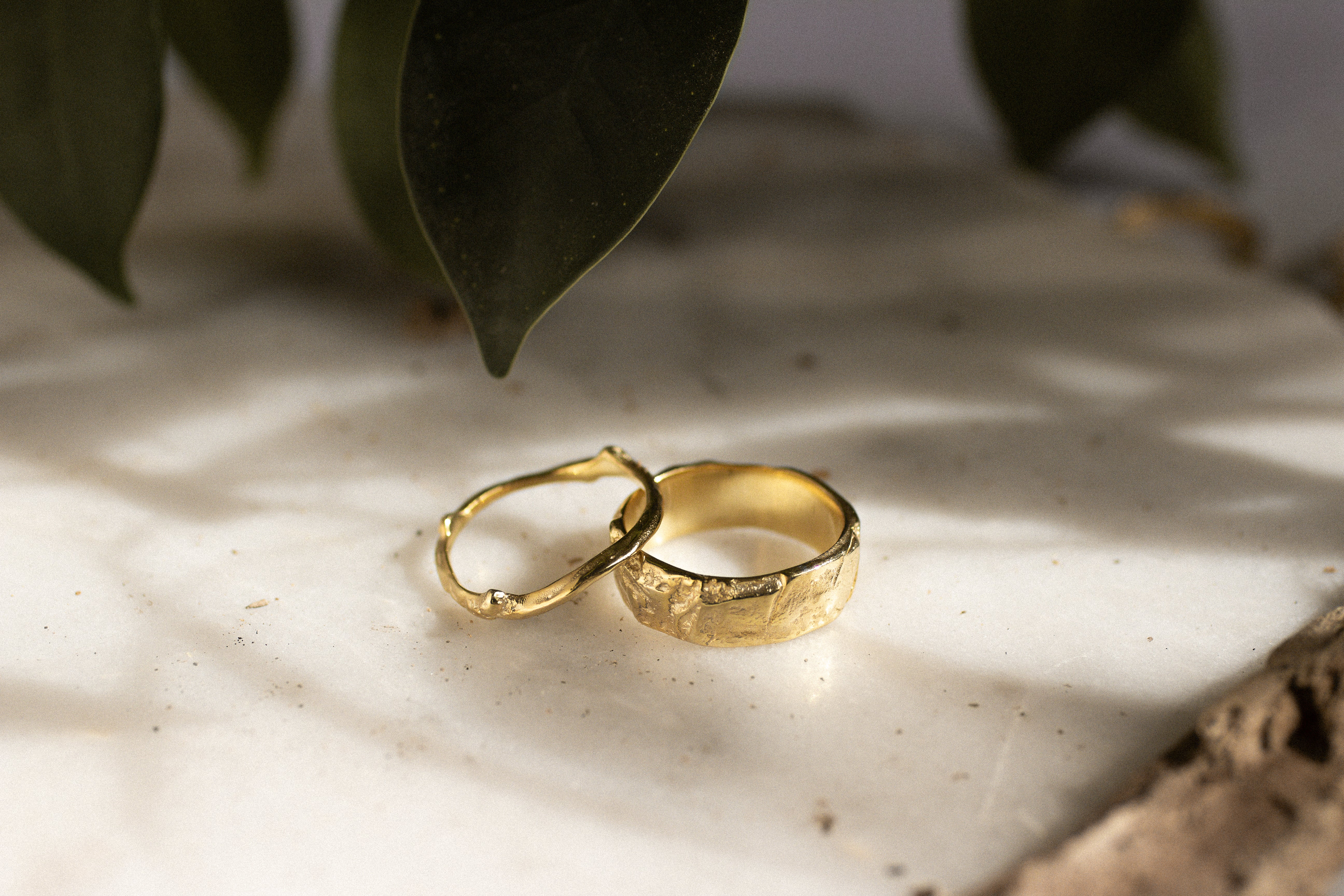Two gold rings on a textured surface with leaves in the background