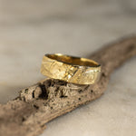 Gold tree bark wedding ring on a piece of bark with a neutral background