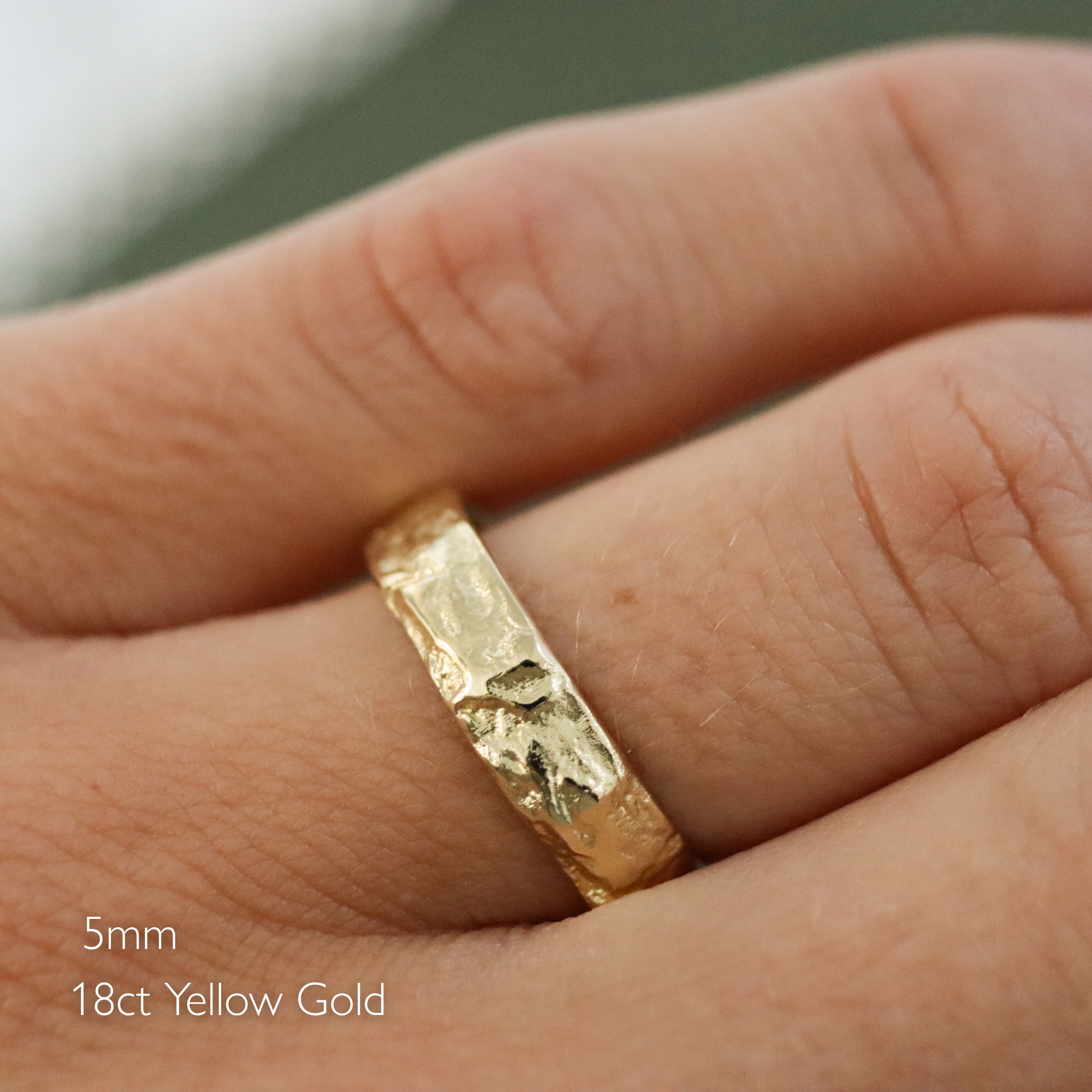 A close-up of a hand wearing a textured yellow gold band ring, with text overlay in the bottom-left corner reading '5mm 18ct Yellow Gold'.