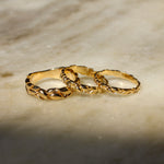Three interlocking textured gold rings displayed on a light beige marble surface with soft shadows.