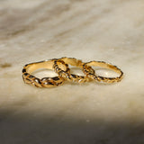 Three interlocking textured gold rings displayed on a light beige marble surface with soft shadows.