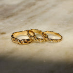 Three interlocking textured gold rings displayed on a light beige marble surface with soft shadows.