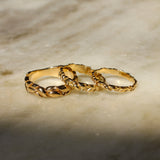 Three interlocking textured gold rings displayed on a light beige marble surface with soft shadows.