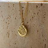gold necklace featuring textured round pendant with compass design against a stone background