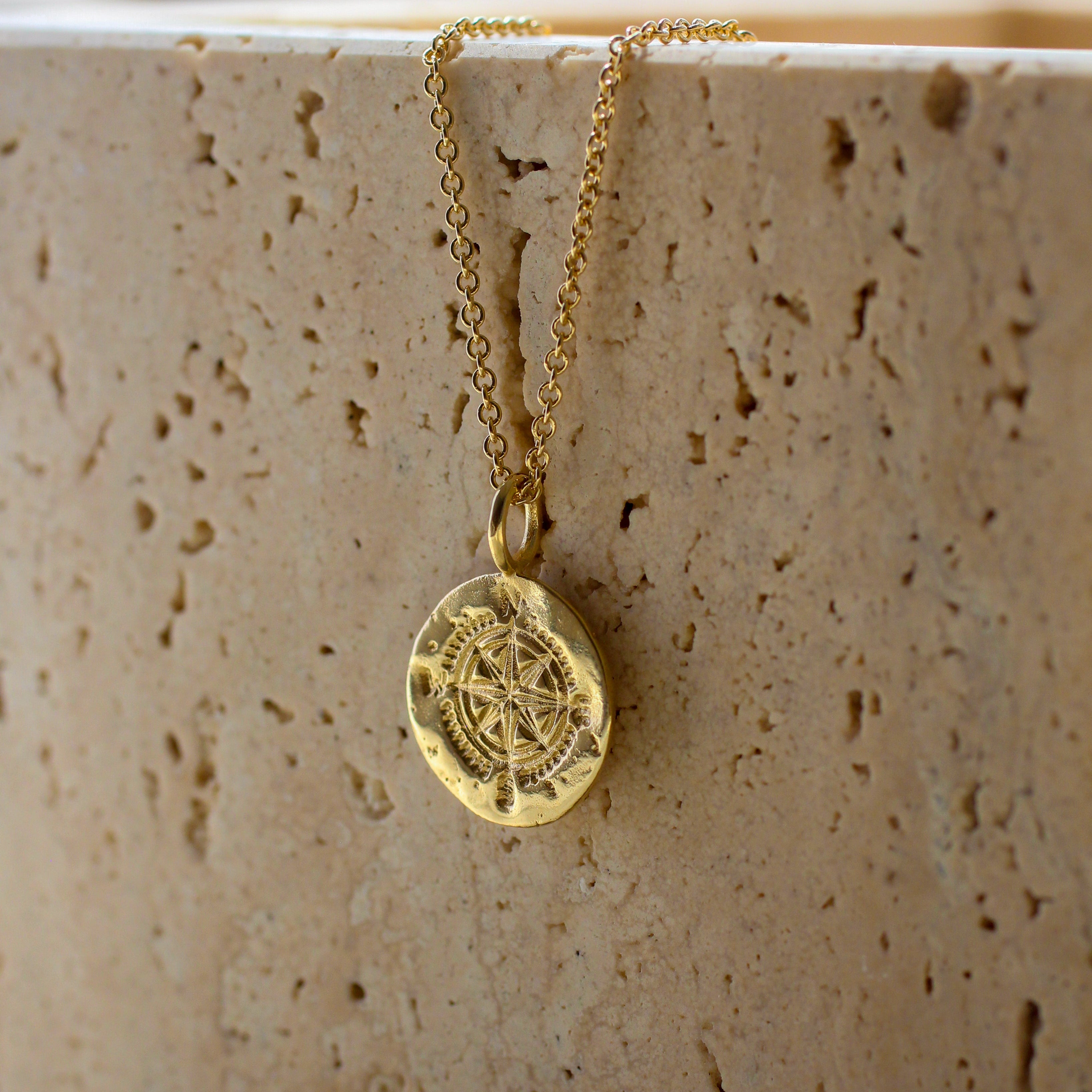 gold necklace featuring textured round pendant with compass design against a stone background