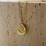 gold necklace featuring textured round pendant with compass design against a stone background