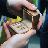hands holding a wooden wedding ring box containing a chunky gold band and smaller wedding ring