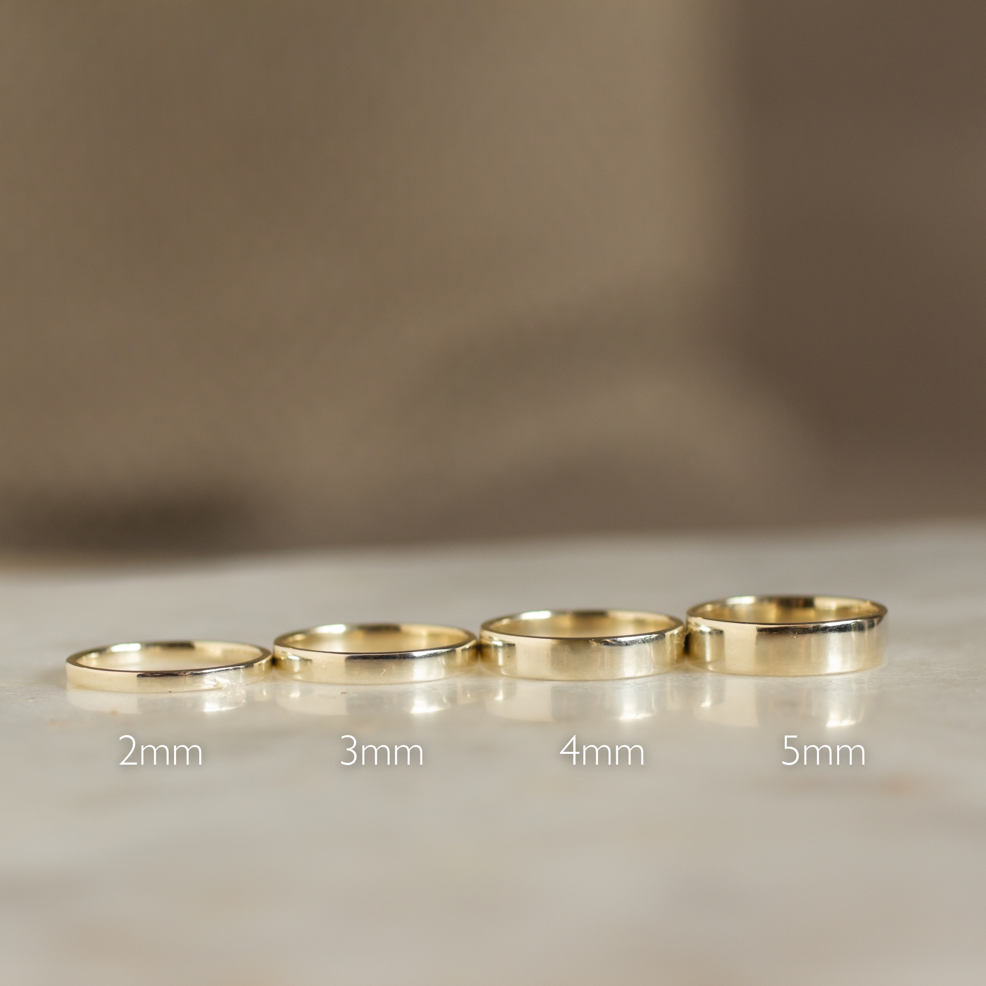 four flat wedding rings in different widths with a neutral background