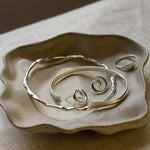Silver jewellery on a textured ceramic dish with a brown background