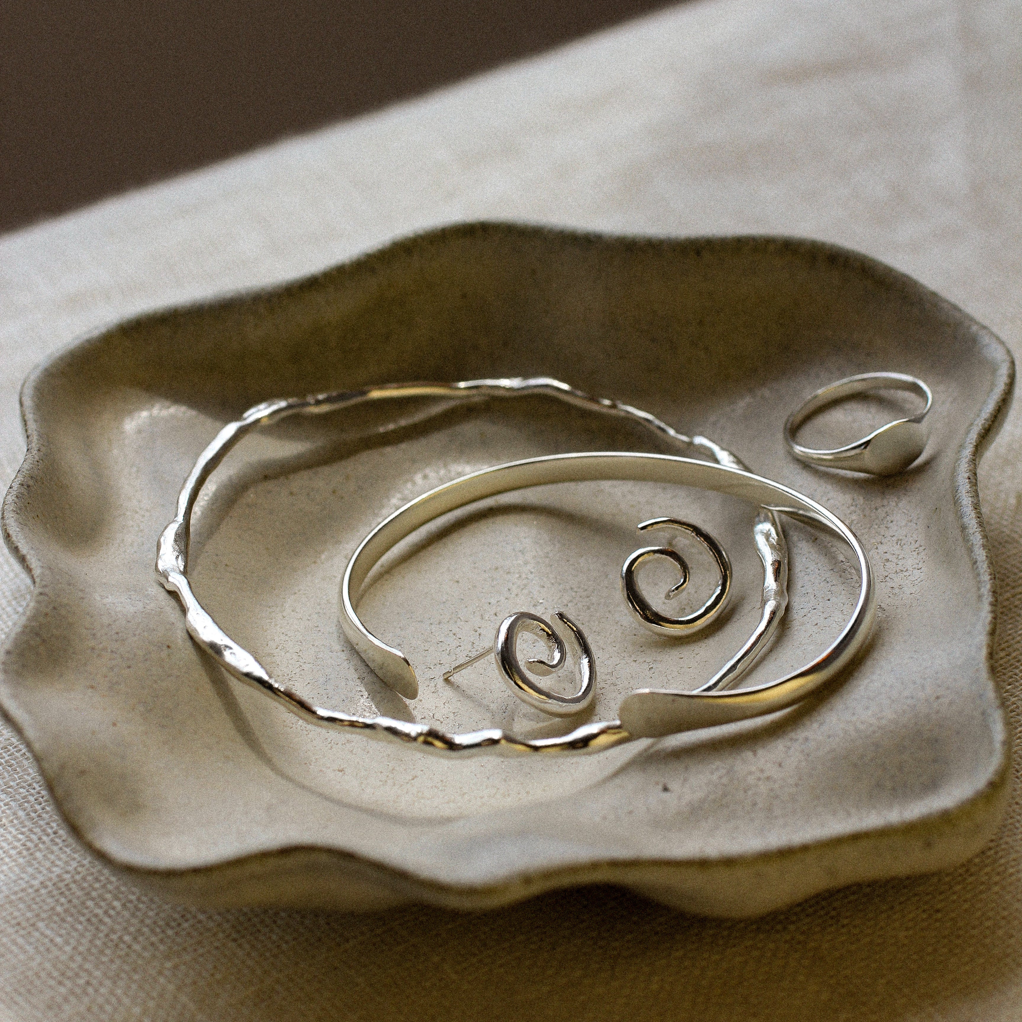 Silver jewellery on a textured ceramic dish with a brown background