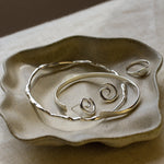 Silver jewellery on a textured ceramic dish with a brown background