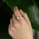 hand wearing a ring engraved with 'Worthy' with leaves in the background