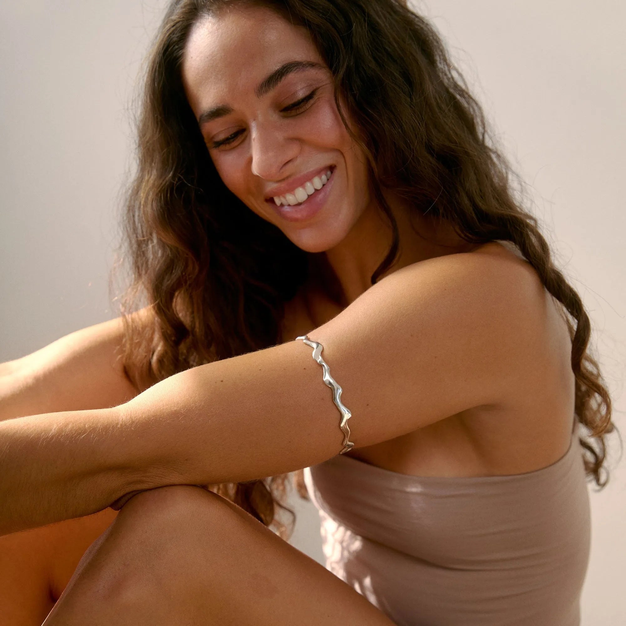 Woman wearing a wavy silver bangle on her upper arm on a wooden floor with a neutral background