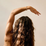Person with long hair and arm raised wearing a silver wavy bangle against a plain background