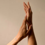 Two hands clasping together against a beige background wearing a delicate silver bracelet