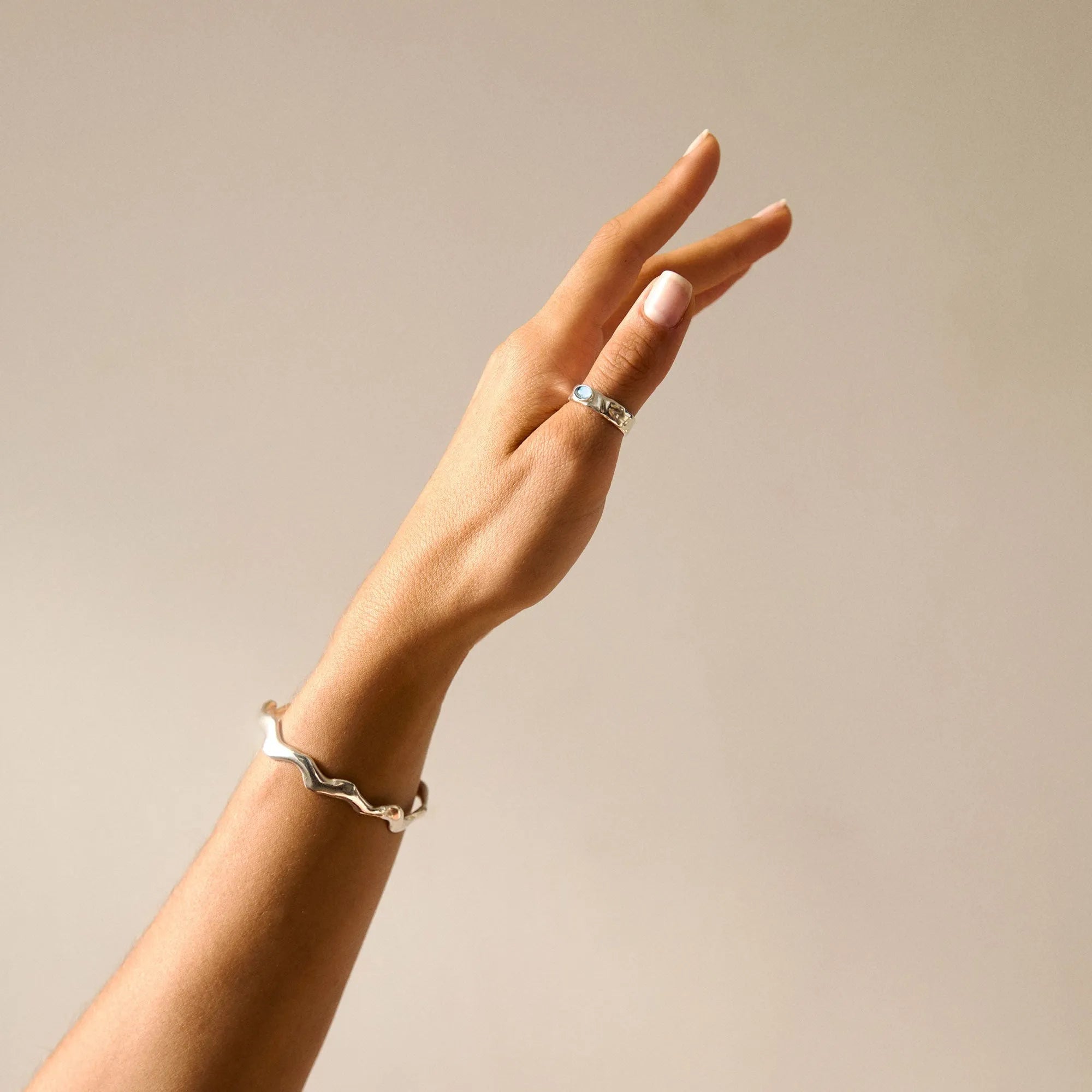 outstretched hand wearing a silver bangle and topaz ring on a beige background