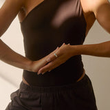 Woman wearing a black one-shoulder top and black pants against a neutral background
