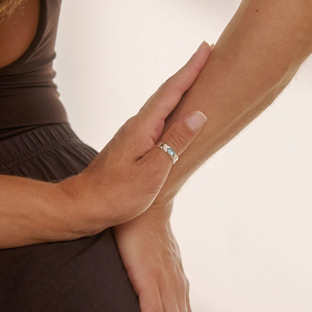 Woman wearing a silver blue topaz ring with her hand on her hip against a neutral background