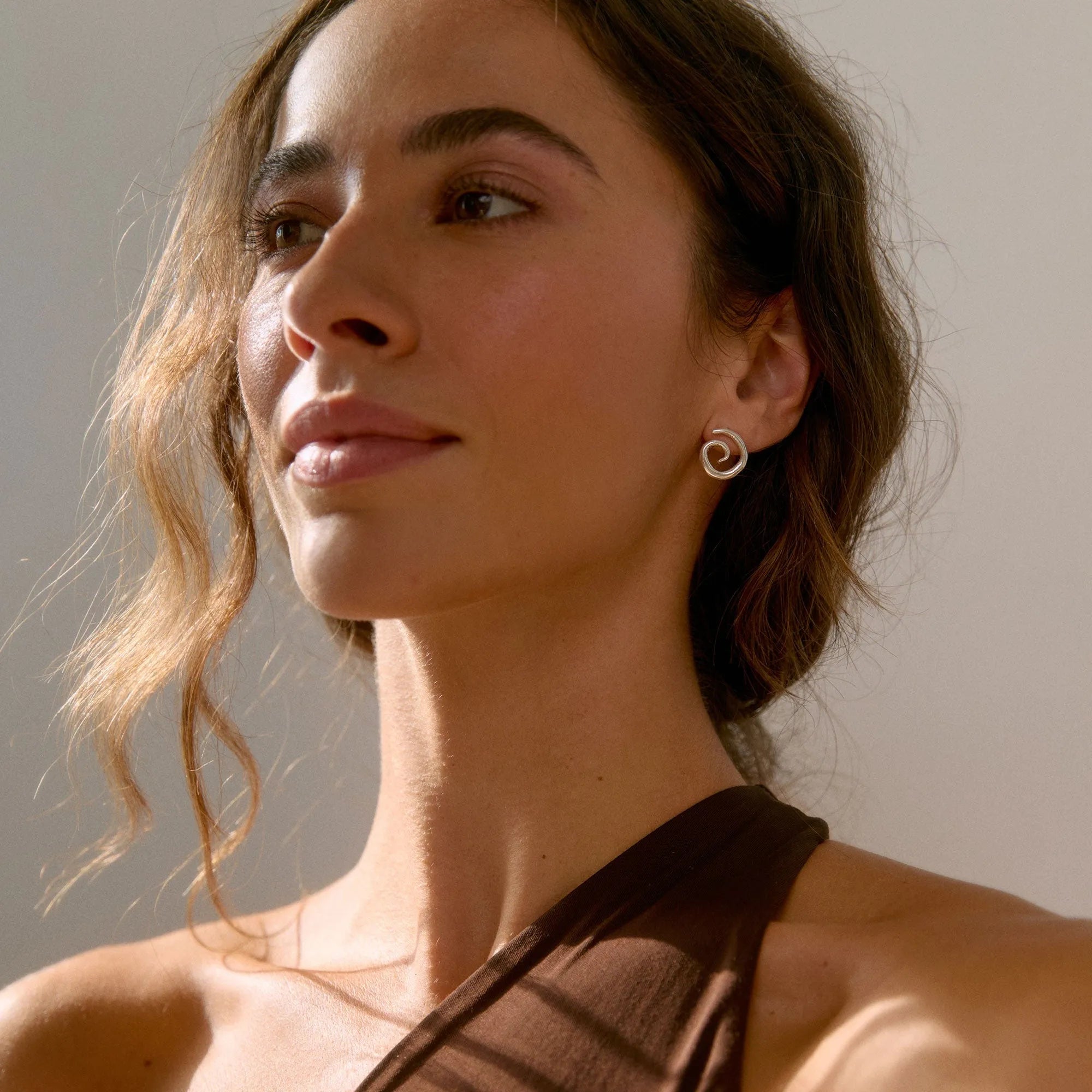 Woman wearing a brown halter top and spiral silver stud earrings with a neutral background