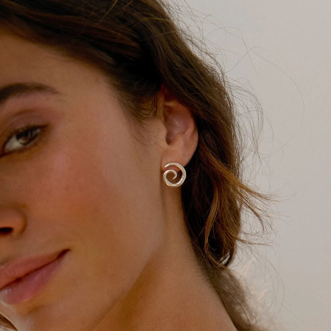 close up of model wearing silver spiral stud earrings against a neutral background