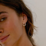 close up of model wearing silver spiral stud earrings against a neutral background